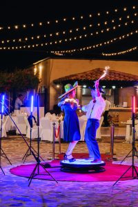 Dancing couple wearing sombreros at outdoor wedding reception under string lights and night sky.