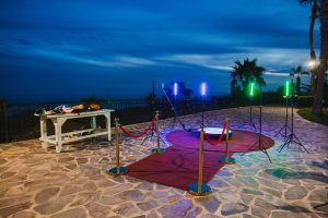 Elegant outdoor wedding photo setup with a red carpet, colorful lighting, and ocean view at dusk.