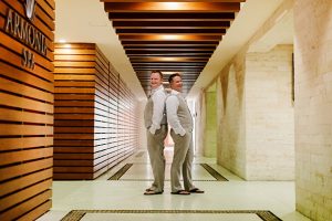 Elegant grooms smiling in modern hotel corridor for wedding photography.