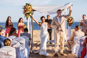 Elegant beach wedding ceremony with bride and groom celebrating by the ocean, surrounded by bridesmaids and guests.