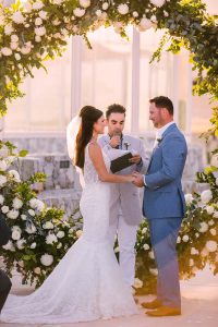 Elegant outdoor wedding ceremony at sunset, bride and groom exchanging vows under floral arch.