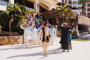 Vibrant Indian wedding procession at a luxury seaside resort with traditional attire and dancing.