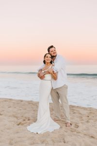 Beautiful couple in wedding attire embracing on the beach at sunset.